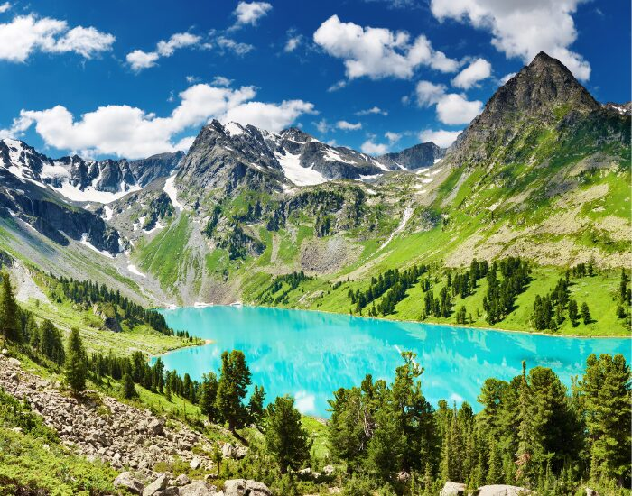Dimitry Pichugin a photo of a turquoise lake surrounded by pine trees and bog rocky mountains
