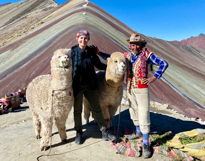 A woman with two alpacas and an local man with a colourful mountain on the background