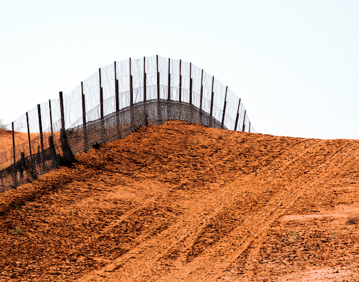 dingo fence High wire pest-exclusion dingo fence running through red dirt outback terrain.