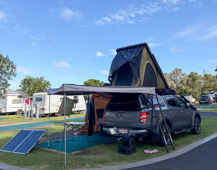 grey 4WD vehicle with a rooftop tent set up at a campsite.