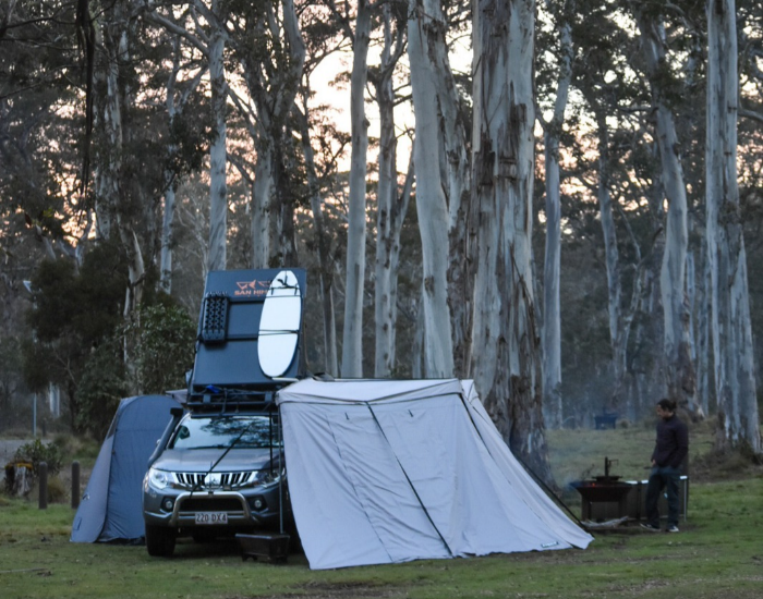 a triton car with a rooftent and a surf board attached to it and an awning